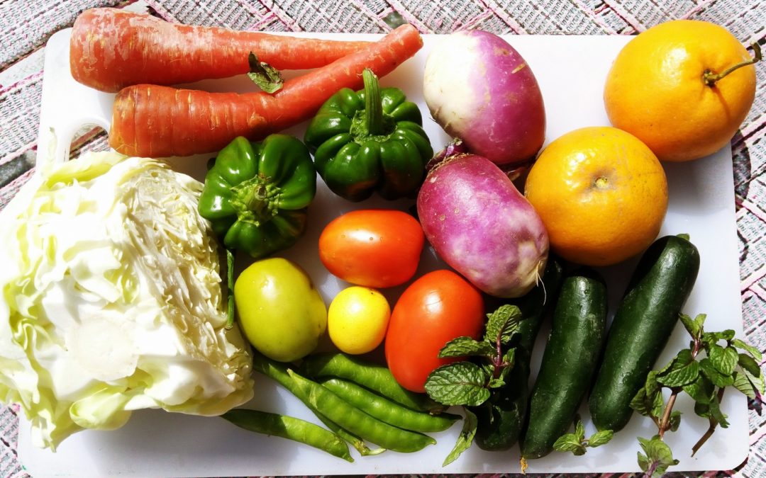 A basket of vegetables: carrots, bell peppers, tomatoes, cucumbers, peas, and radishes.